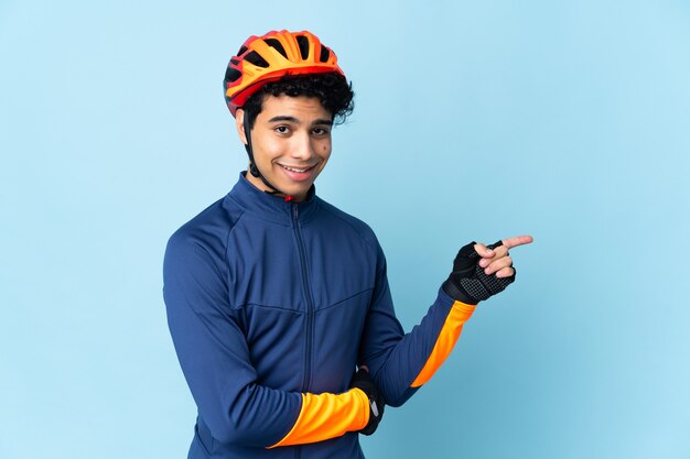 Hombre ciclista venezolano aislado en la pared azul que señala el dedo hacia el lado