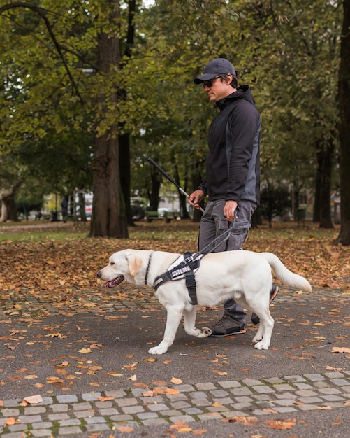 Hombre ciego caminando con la ayuda de un perro guía a través del parque de otoño