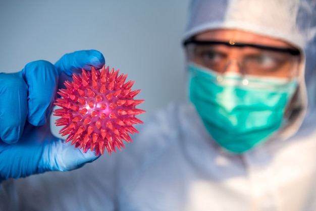 Foto hombre científico con traje protector sosteniendo un modelo rojo de coronavirus