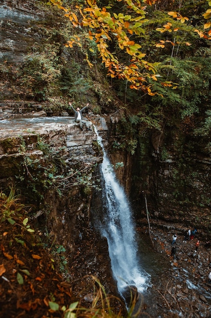 Hombre en la cima de la cascada en el bosque de otoño