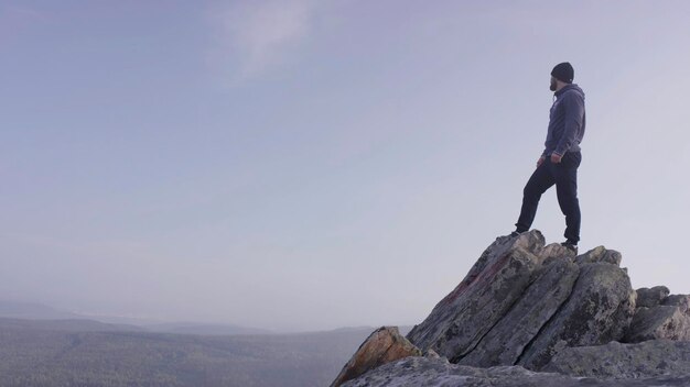 Hombre en la cima de la montaña un joven atlético está de pie en una roca alta