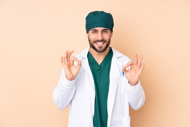 Hombre cirujano en la pared de color beige que muestra un signo bien con los dedos