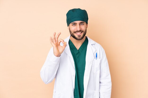 Foto hombre cirujano en la pared de color beige que muestra un signo bien con los dedos