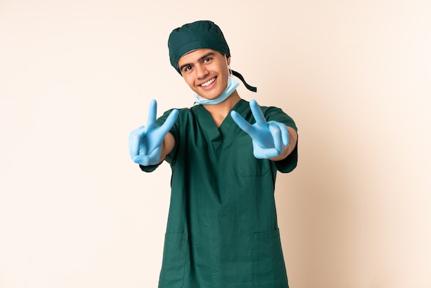 Hombre cirujano en uniforme azul sobre fondo aislado sonriendo y mostrando el signo de la victoria