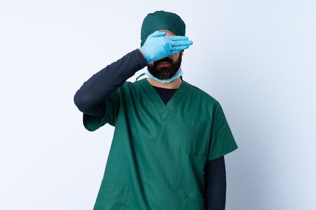 Hombre cirujano en uniforme verde sobre pared aislada que cubre los ojos con las manos. No quiero ver algo