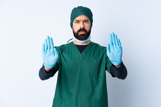 Hombre cirujano en uniforme verde sobre pared haciendo gesto de parada y decepcionado