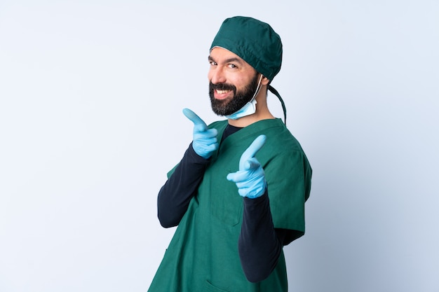 Hombre cirujano en uniforme verde sobre pared sorprendido y apuntando al frente