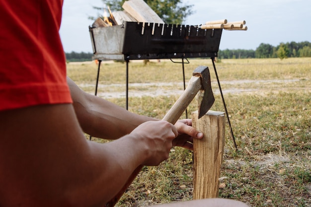 Un hombre en una ciudad de acampada corta leña con un hacha para hacer una barbacoa