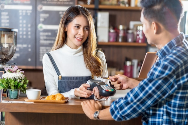 Foto hombre cliente asiático pagando con tarjeta de crédito a través de tecnología nfs sin contacto a asian barista