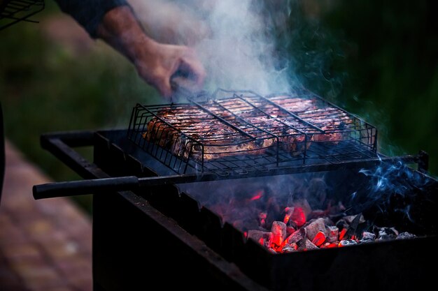 un hombre cocina carne en una parrilla en la que las brasas se queman en la naturaleza