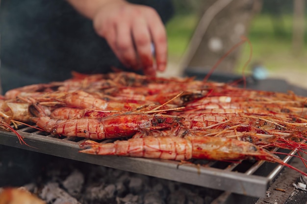 El hombre cocina grandes langostinos de camarón en un fuego abierto en la parrilla con barbacoa de humo al aire libre