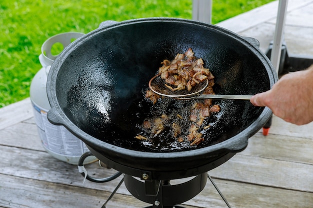 Un hombre cocina tocino al aire libre en un caldero.