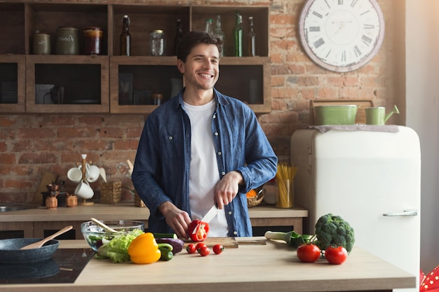 Hombre cocinando comida deliciosa y saludable en la cocina del desván en casa en un día soleado. Preparar ensalada de verduras para la familia, espacio de copia