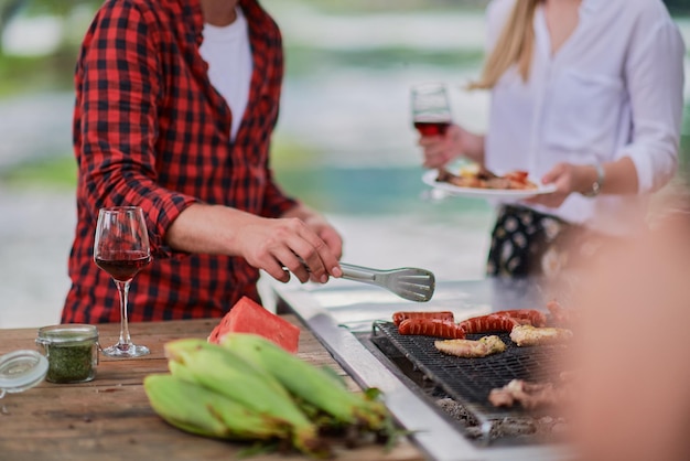 Hombre cocinando comida sabrosa en la parrilla de la barbacoa para una cena francesa al aire libre cerca del río en una hermosa noche de verano en la naturaleza