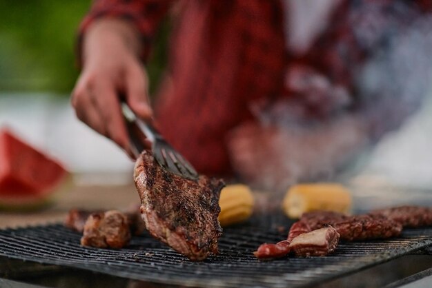 Hombre cocinando comida sabrosa en la parrilla de la barbacoa para una cena francesa al aire libre cerca del río en una hermosa noche de verano en la naturaleza