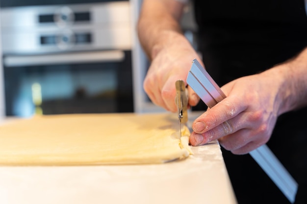 Hombre cocinando croissants caseros midiendo hojaldre y haciendo cortes en casa