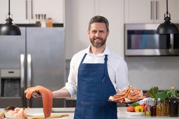 Hombre cocinando garra de cangrejo y pescado Hombre hispano en la cocina con mariscos Hombre maduro cocinando pierna de cengrejo Dieta de alimentos saludables Hombre cocinado mariscos Menú de pescado con mariscas Cangrejo Rey de Alaska