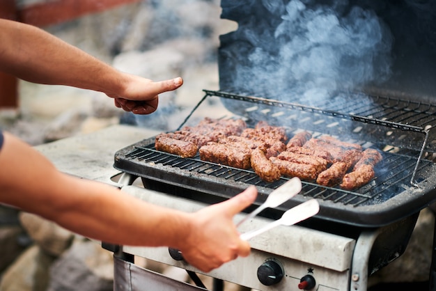 Hombre cocinando mititei rumano en parrilla