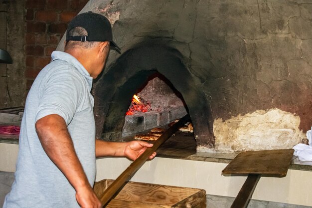 Hombre cocinando pan de manera artesanal, en un horno de leña en forma de cúpula, en Chilca - Perú