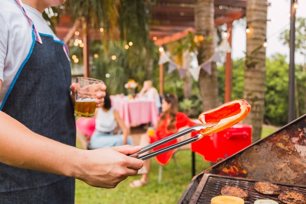 Foto hombre cocinando verduras y hamburguesas para la cena al aire libre.