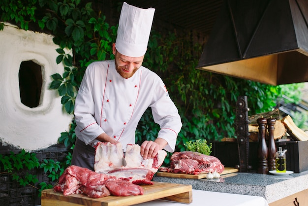 Un hombre cocinero corta la carne con un cuchillo en un restaurante.