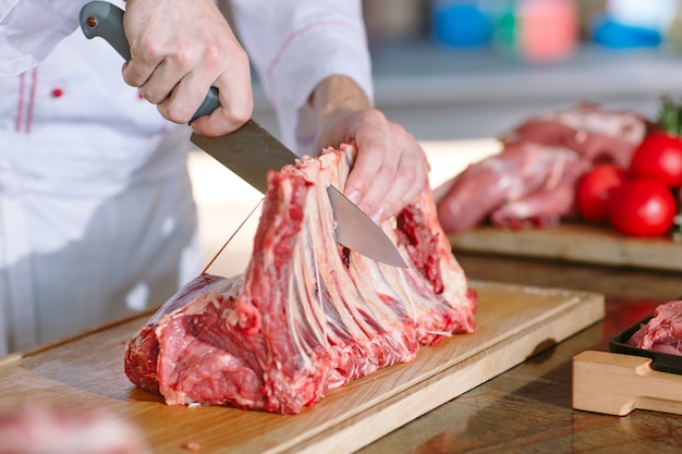 Un hombre cocinero corta la carne con un cuchillo en un restaurante.