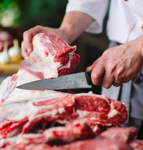 Un hombre cocinero corta la carne con un cuchillo en un restaurante.