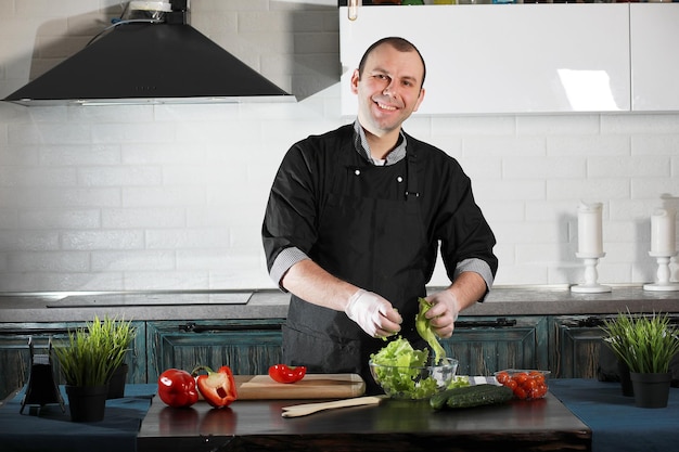 Hombre cocinero preparando comida en la mesa de la cocina de verduras