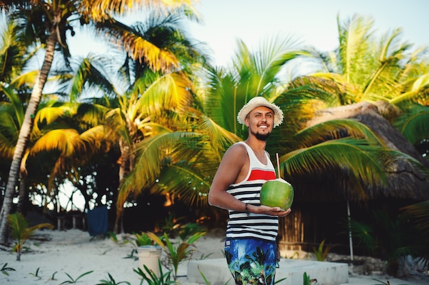 Hombre con coco en la playa tropical en un día soleado de verano durante las vacaciones