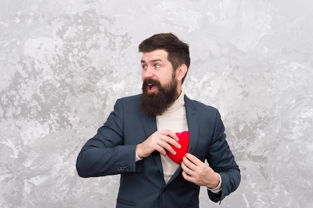 Hombre codicioso que oculta sentimientos. Fiesta de San Valentín. Un apuesto hombre confiado tiene un corazón rojo. Empresario amor símbolo día de san valentín. Listo para una cita romántica. Presente romántico. novio romántico.