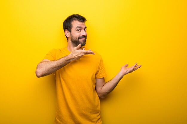 Hombre en color amarillo vibrante aislado que extiende las manos hacia un lado para invitar a venir