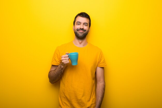 Hombre en el color amarillo vibrante aislado que sostiene el café caliente en la taza de papel para llevar