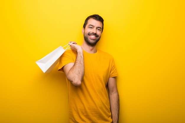 Hombre en el color amarillo vibrante aislado que sostiene muchos bolsos de compras