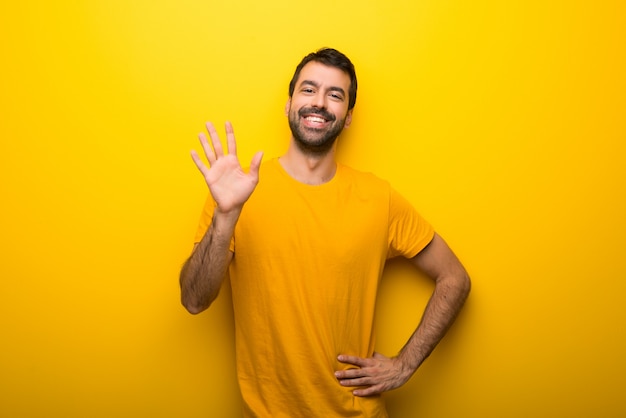 Hombre en color amarillo vibrante aislado saludando con la mano con expresión feliz