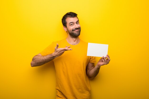 Hombre en color amarillo vibrante aislado sosteniendo un cartel blanco vacío para insertar un concepto