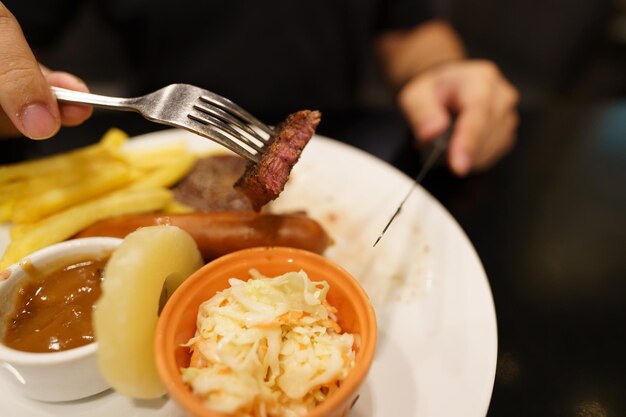 Hombre comiendo carnes a la parrilla estaca del plato mano sujetando cuchillo y tenedor cortando bistec de ternera a la parrilla