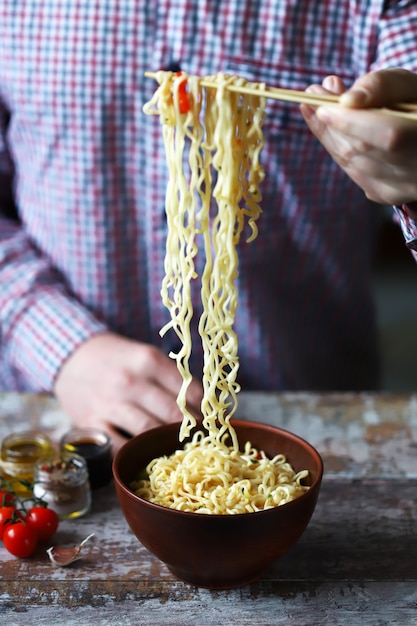 Hombre comiendo fideos con palillos. Fideos chinos.