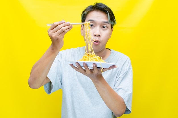 Un hombre comiendo fideos sobre un fondo amarillo hombre asiático disfrutando de fideos