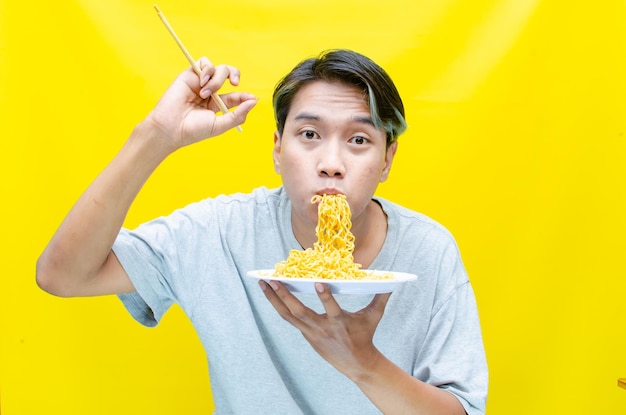 Un hombre comiendo fideos sobre un fondo amarillo hombre asiático disfrutando de fideos