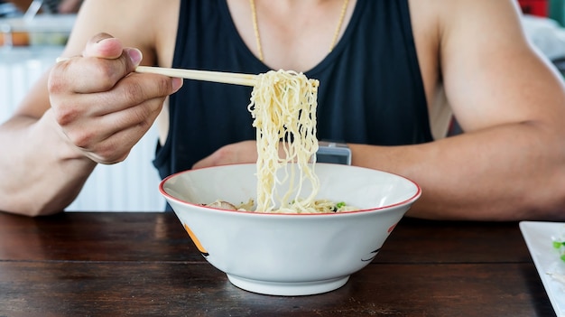 Hombre comiendo fideos tailandeses en una cantina.