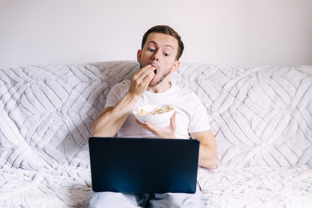 Hombre comiendo palomitas de maíz viendo rápidamente una película en una laptop