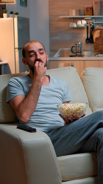 Hombre comiendo palomitas de maíz y viendo la televisión, disfrutando de un bocadillo de medianoche