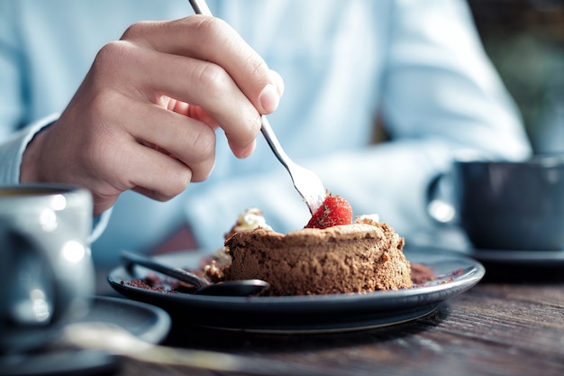 Hombre comiendo un pastel con fresas en un café, close-up