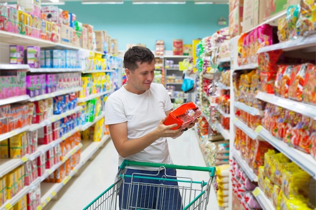 Un hombre comprando en una tienda de comestibles con un carrito lleno de comida.