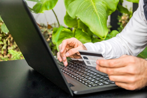 Hombre de compras en línea con su tarjeta de crédito desde su computadora portátil. Primer plano de un hombre de compras en línea usando la computadora portátil con tarjeta de crédito