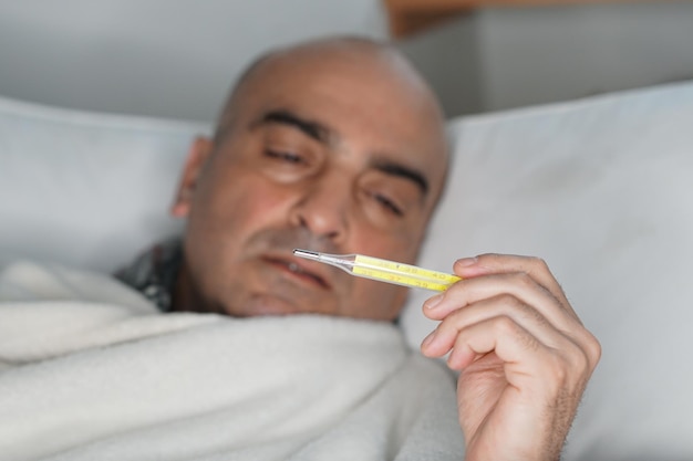 Hombre comprobando la temperatura mientras está acostado en la cama en casa