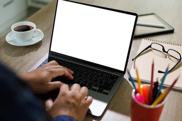 Hombre de computadora de pantalla en blanco de maqueta que usa una computadora portátil en el escritorio en una computadora portátil de oficina con pantalla de espacio de copia en blanco para su mensaje de texto publicitario