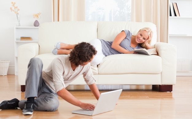 Hombre con una computadora portátil mientras su novia está sosteniendo un libro