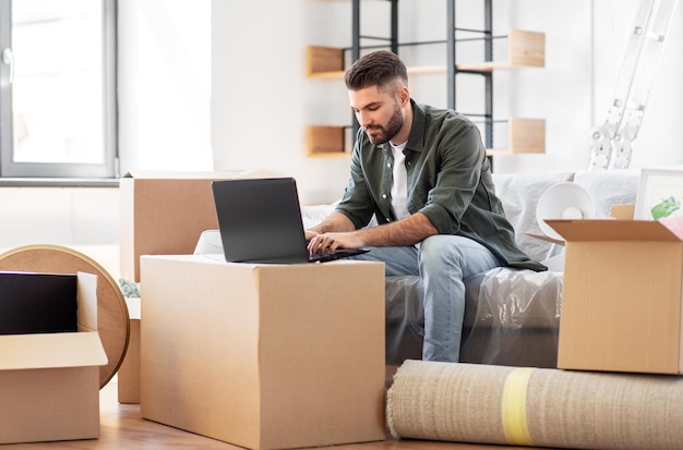 hombre con computadora portátil y mudándose a una nueva casa