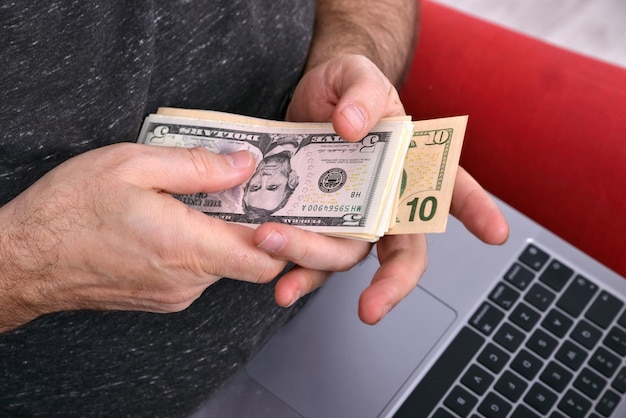 Hombre con computadora portátil en el regazo y dinero en manos concepto de negocio en línea de primer plano